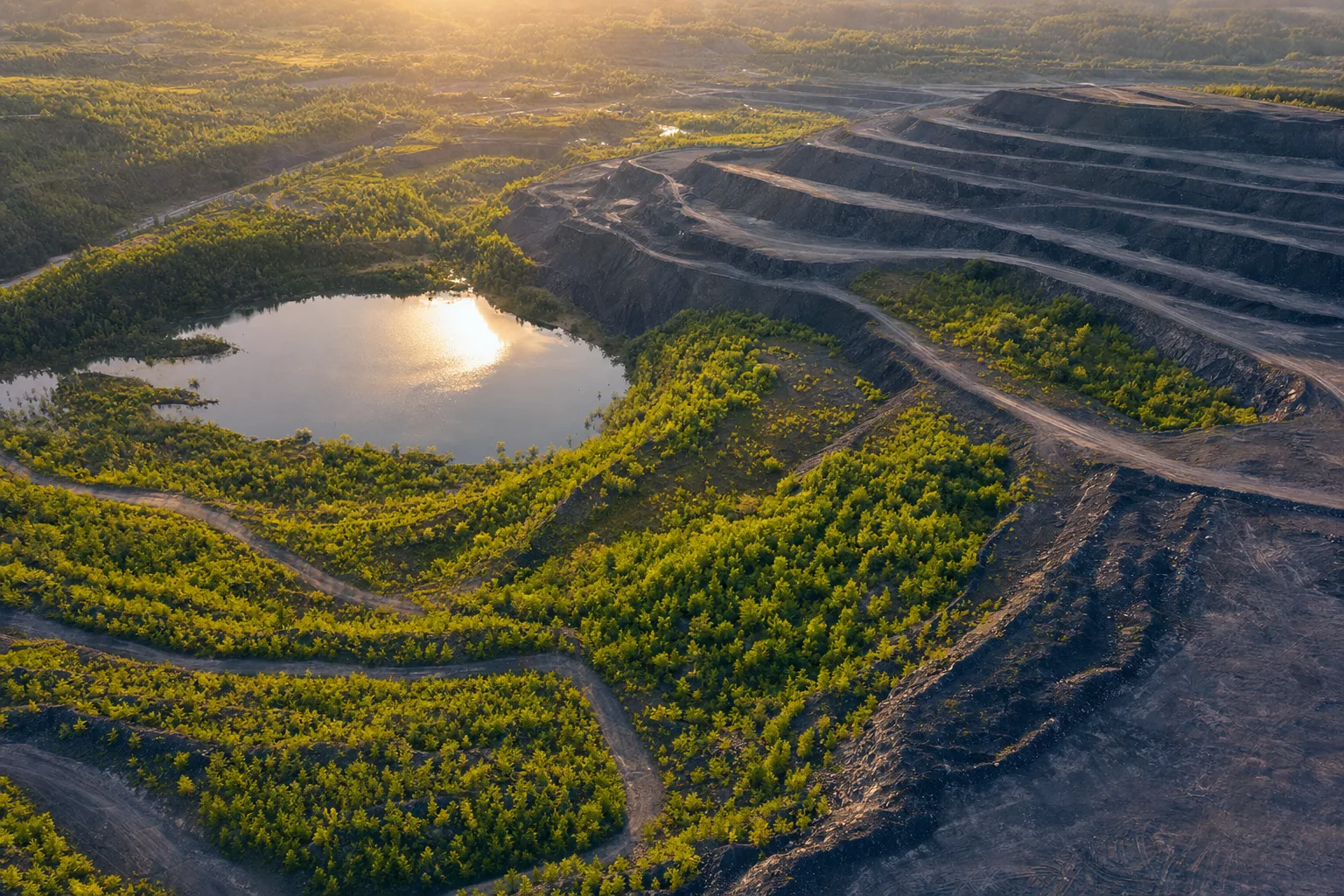 Aerial view of a partially rehabilitated former mining landscape with vegetation returning to lower terraces